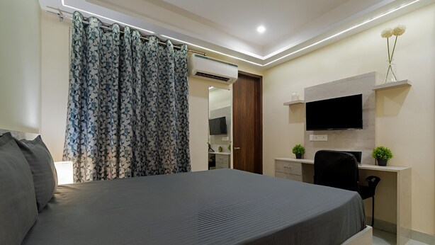 A modern bedroom with a bed, a desk, a TV, and an air conditioning unit. - Saunter living (Gurugram)