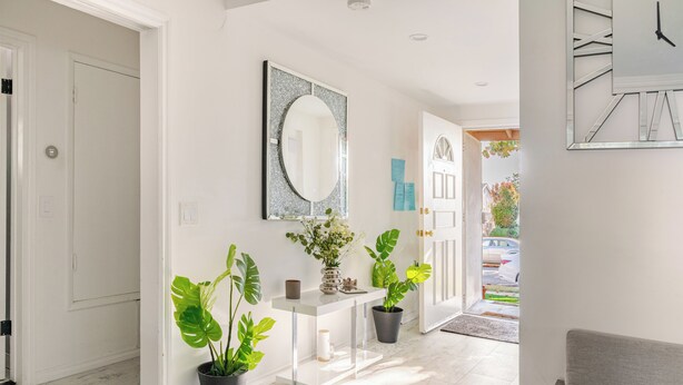 A hallway with a white console table, two potted plants, a mirror, and a clock on the wall. - Hideaway Haven near LAX, Sofi Stadium, the Forum. (Inglewood)