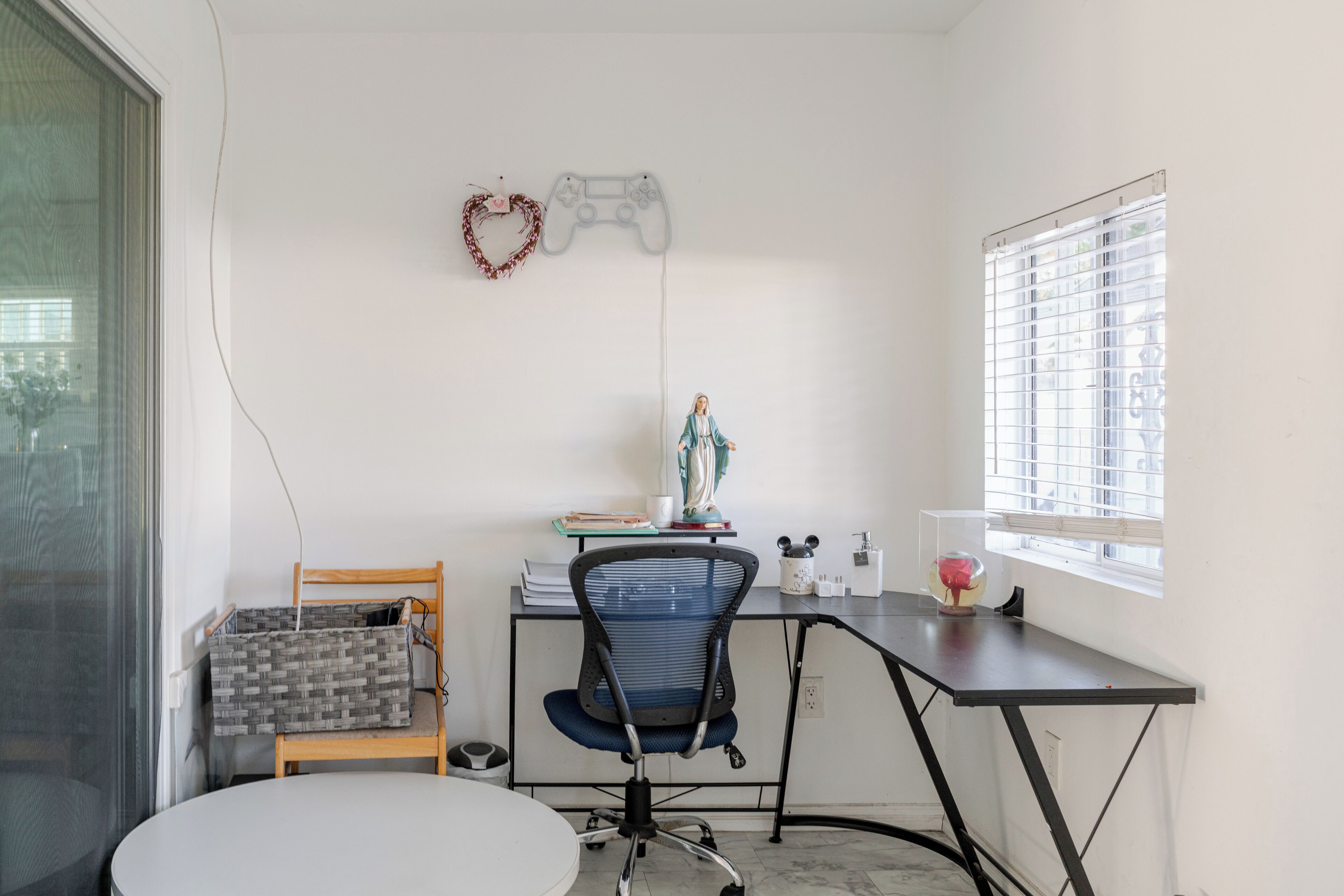 Une pièce comprenant un bureau, une chaise et une petite table. Il y a une fenêtre avec des stores, une décoration en forme de cœur et une figurine posée sur le bureau.