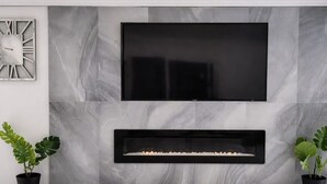 A modern living room with a large flat-screen TV mounted above a fireplace, marble walls, and two potted plants. - Hideaway Haven near LAX, Sofi Stadium, the Forum. (Inglewood)