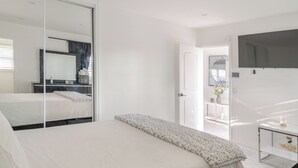 A modern bedroom with a large bed, a bedside table, a mirror, and a TV mounted on the wall. - Hideaway Haven near LAX, Sofi Stadium, the Forum. (Inglewood)
