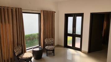A spacious room with a large window, two chairs, a round table, and a ceiling fan.