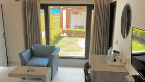 Une chambre d’hôtel moderne équipée d’un canapé, d’une petite table, d’un bureau avec un ordinateur et d’une grande fenêtre donnant sur l’extérieur.