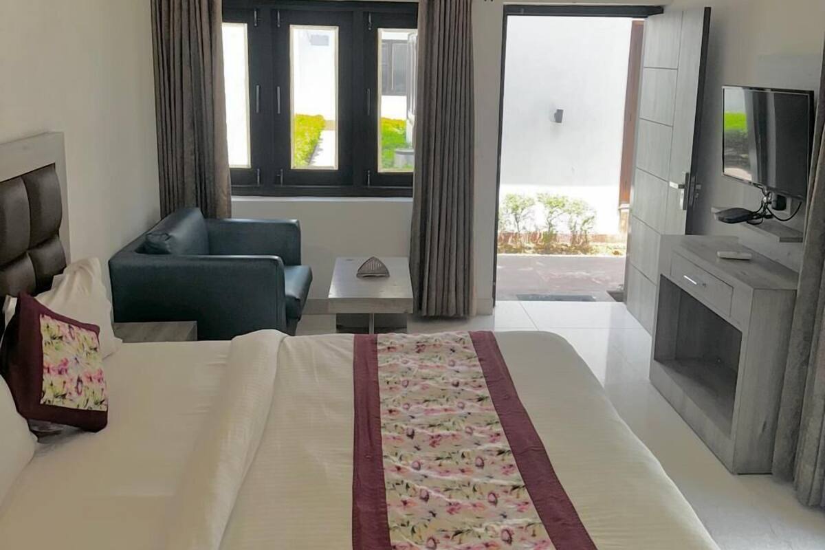 A hotel room with a large bed, a sofa, a TV, and a balcony with curtains.