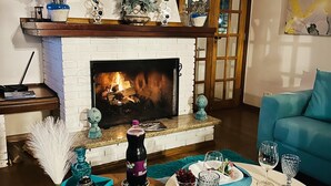 A cozy living room with a fireplace, decorative flowers, a dining table set with plates and glasses, and a blue sofa. - Pousada Blue Village (Campos do Jordão)