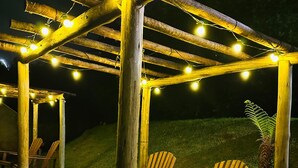A wooden pergola with string lights, two Adirondack chairs, and a small fire pit. - Pousada Blue Village (Campos do Jordão)