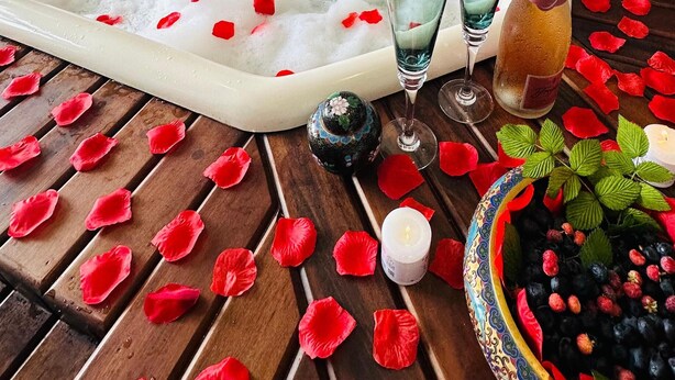 A spa area with a hot tub surrounded by rose petals, candles, and a bowl of berries. - Pousada Blue Village (Campos do Jordão)