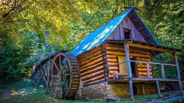 Una cabana de fusta rústica amb fonaments de pedra, rodes de fusta grans i teulada metàl·lica.