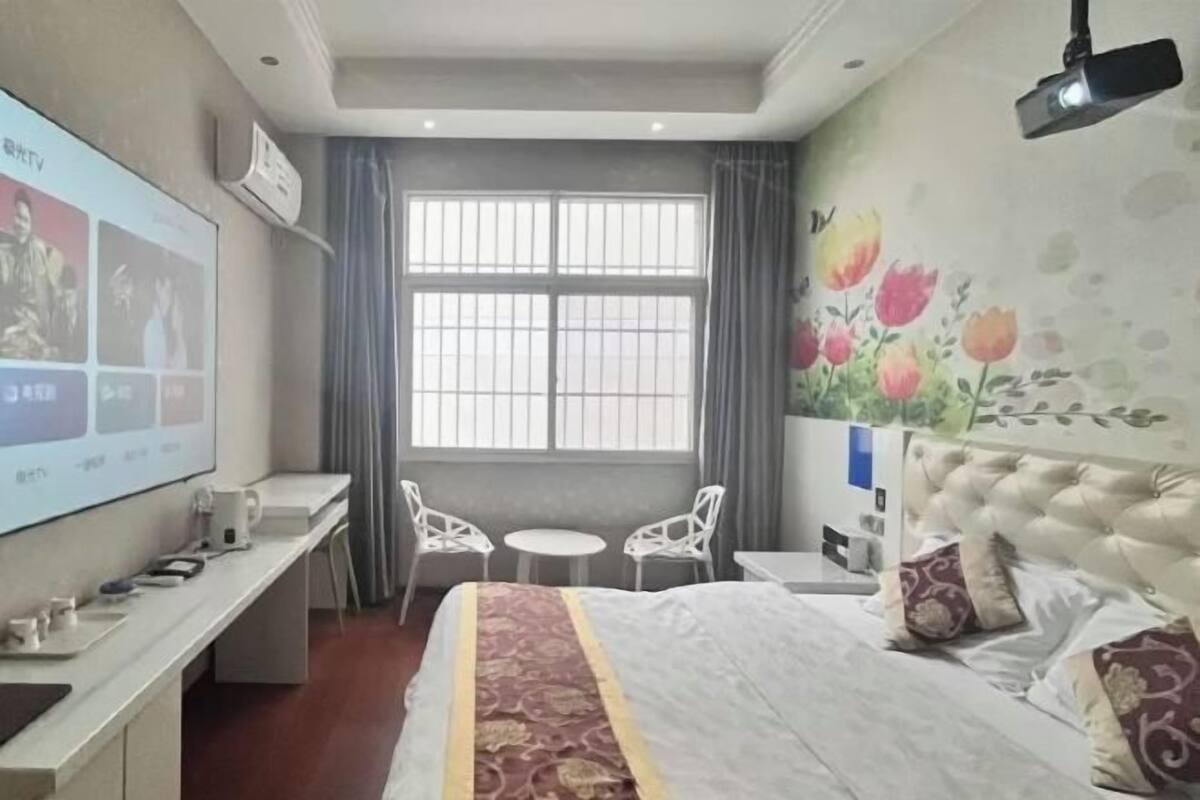 Habitación de hotel con cama, escritorio con computadora, televisor, dos sillas, una mesita y ventana con cortinas.