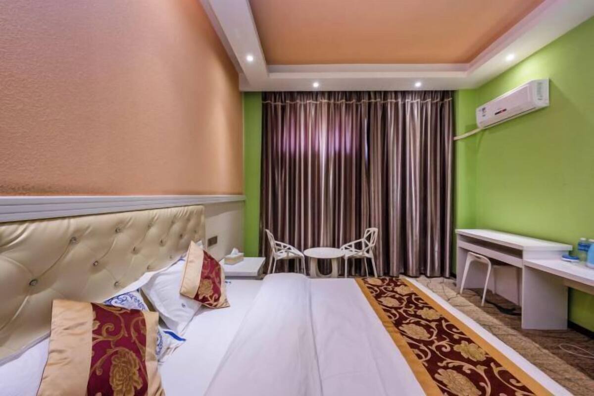 Habitación de hotel con cama, escritorio, dos sillas, cortina y unidad de aire acondicionado.