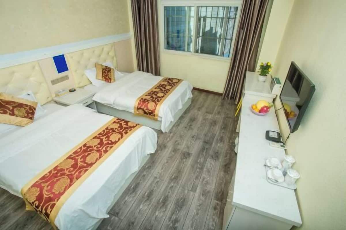 Habitación de hotel con dos camas, un escritorio con computadora y teléfono, una ventana con cortinas y una pequeña planta.