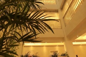 Ein mehrgeschossiges Atrium mit einer zentralen Säule, Topfpflanzen und warmer Innenbeleuchtung.