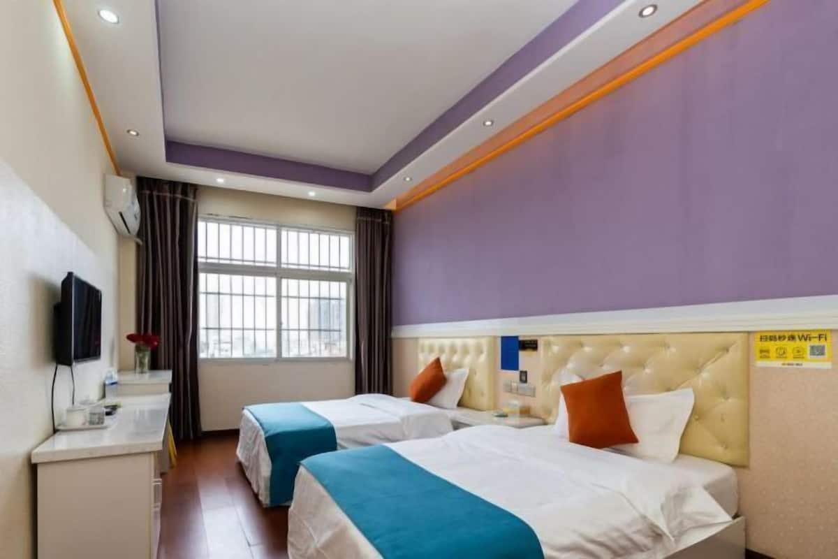 Habitación de hotel con dos camas, un escritorio, televisor y ventana.
