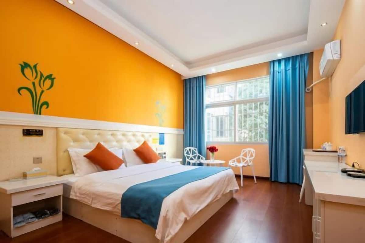 Una habitación de hotel con cama, escritorio, silla, ventana con cortinas y un adorno en la pared.