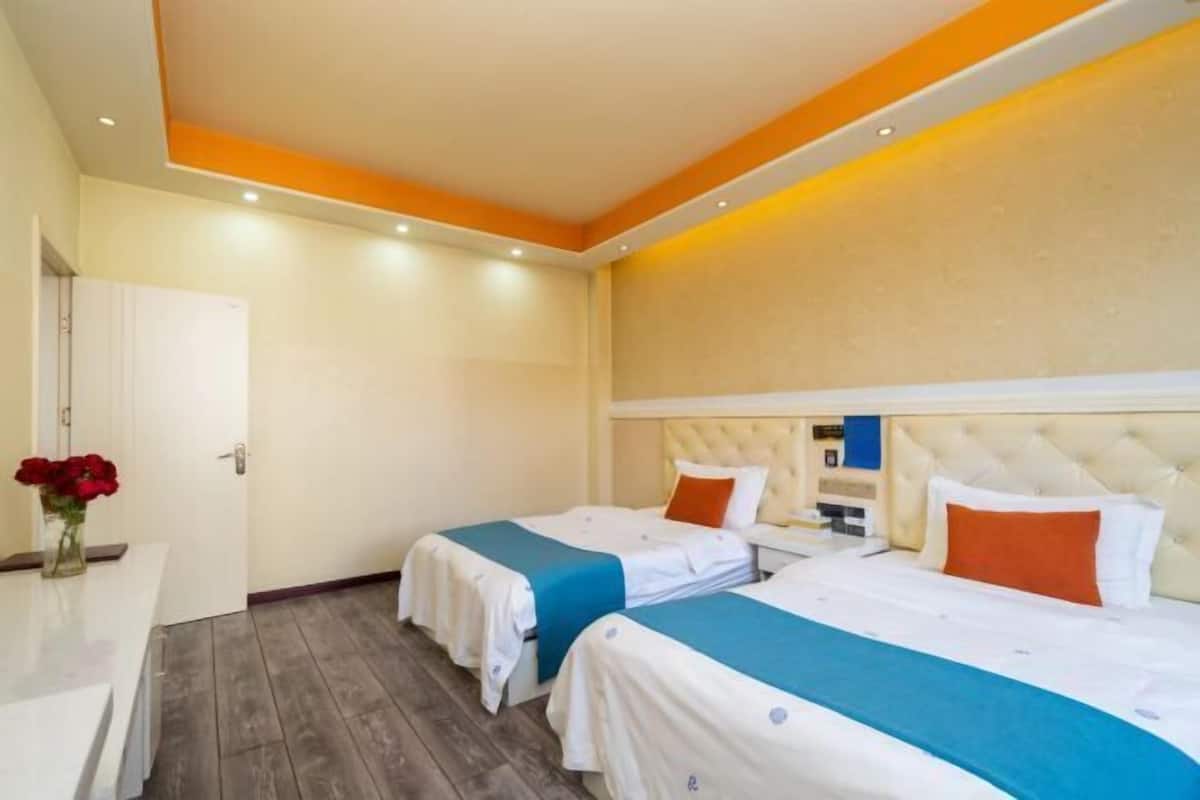 Una habitación de hotel con dos camas, un escritorio y un jarrón de flores rojas.