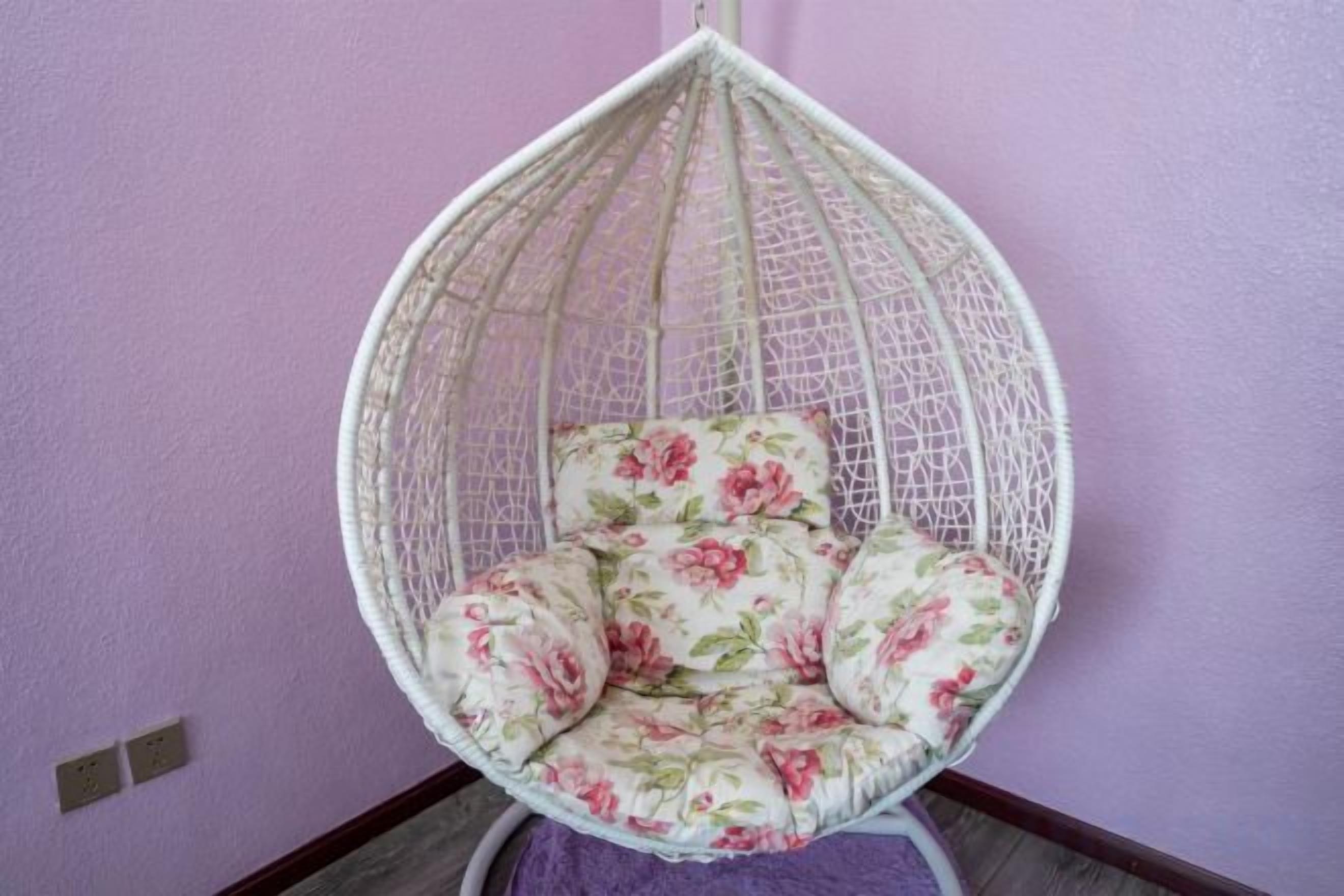 A hanging chair with floral upholstery against a purple wall.