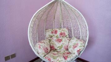 A hanging chair with floral upholstery against a purple wall.