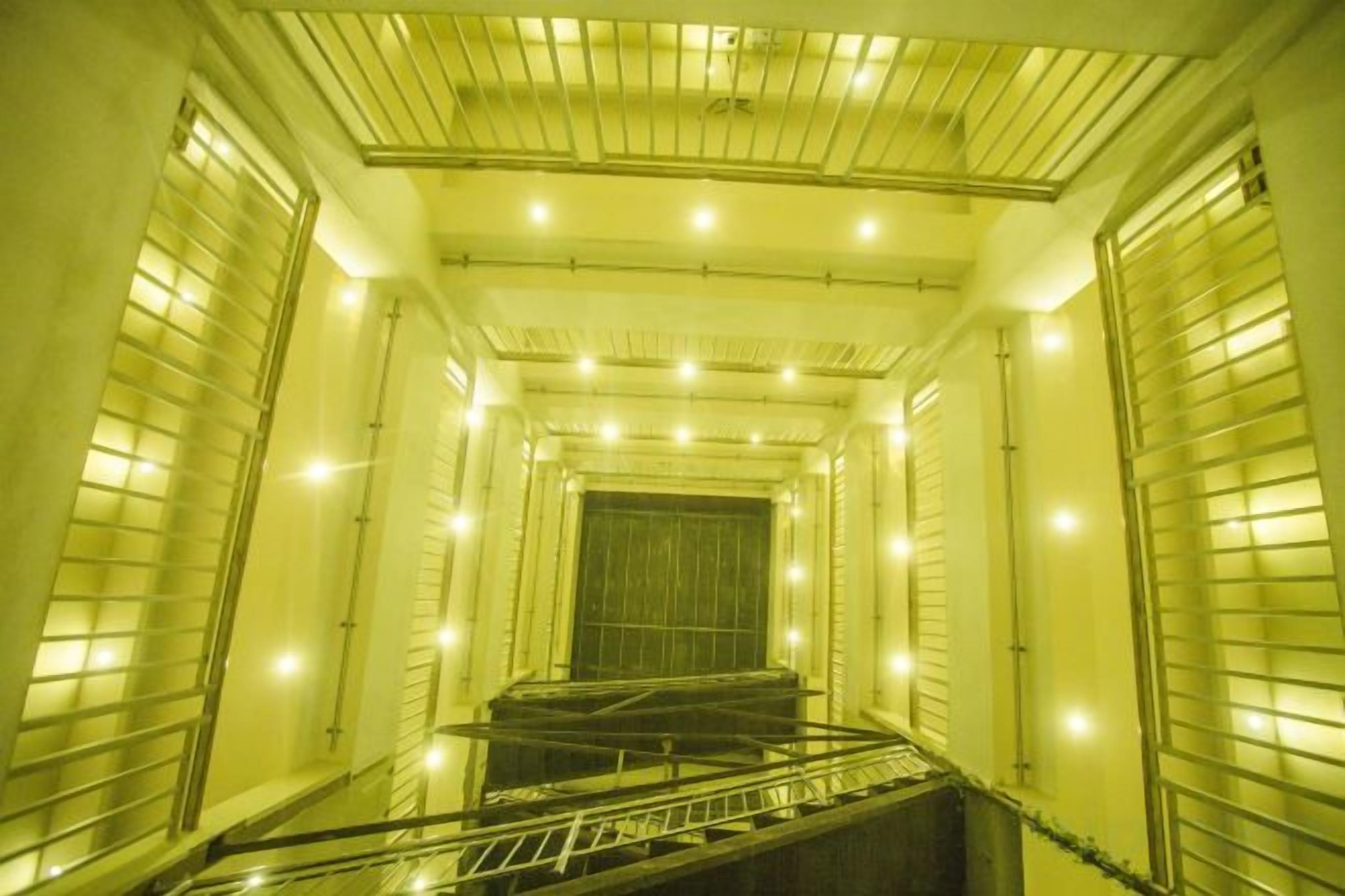 A narrow, enclosed stairwell with metal railings and a series of lights along the ceiling.