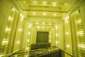 Un escalier étroit et fermé, doté de rampes métalliques et d’une série de luminaires le long du plafond.
