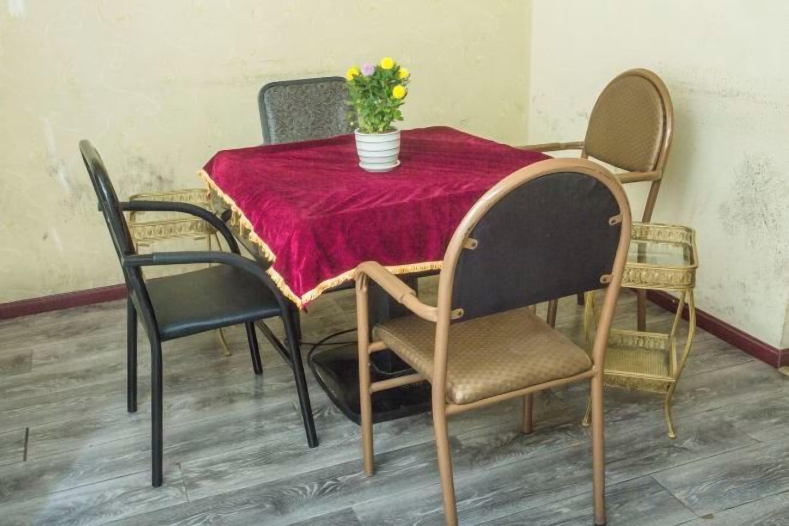 A dining table with a red tablecloth, surrounded by four chairs, one of which is cushioned.