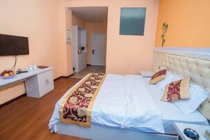 Un dormitorio con cama, mesita de noche, televisor y puerta que da a otra habitación.
