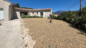 Una casa con tetto in tegole, vialetto sterrato e giardino con diverse piante.