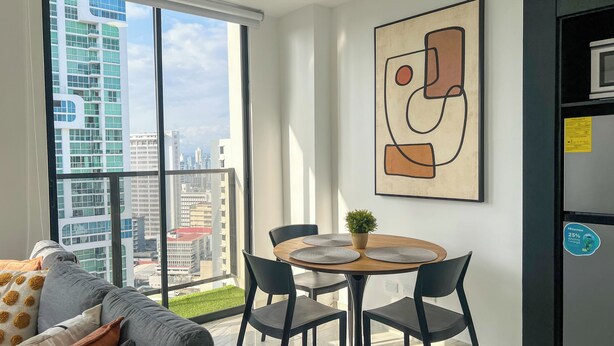 A modern living room with a large window, a dining area with a round table, and a city view.