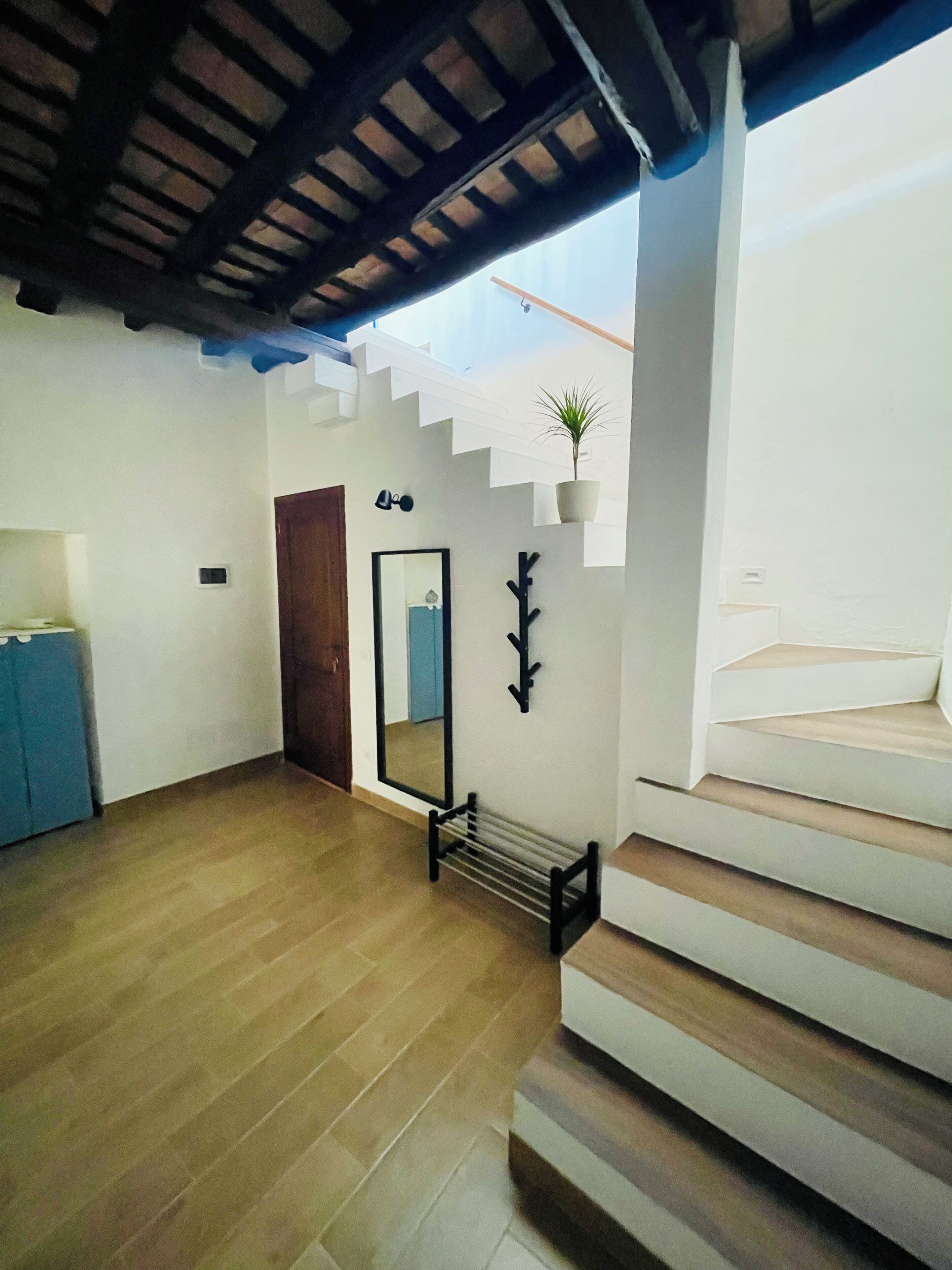 Un intérieur moderne avec un plancher en bois, un escalier, un miroir et une plante en pot.