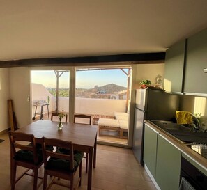 A dining area with a table and chairs, a kitchen with a sink and cabinets, and a sliding glass door leading to an outdoor patio.