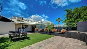 Un jardin avec une terrasse, une pelouse et une clôture.