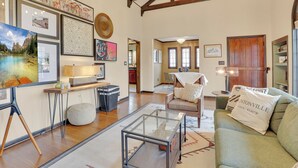 Un salón amplio con un sofá grande, una mesa de centro de vidrio y un comedor con mesa y sillas de madera. Se observan cuadros enmarcados en las paredes y un candelabro colgando del techo.