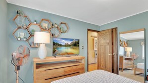 Un dormitorio con cama, cómoda de madera, televisión, ventilador y espejo.