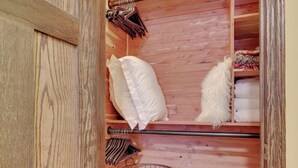 Un interior de madera con un estante metálico, almohadas blancas y una cesta de metal.