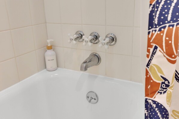 Ein Badezimmer mit einer weißen Badewanne, einem Handseifen-Spender und einer Duschbrause.