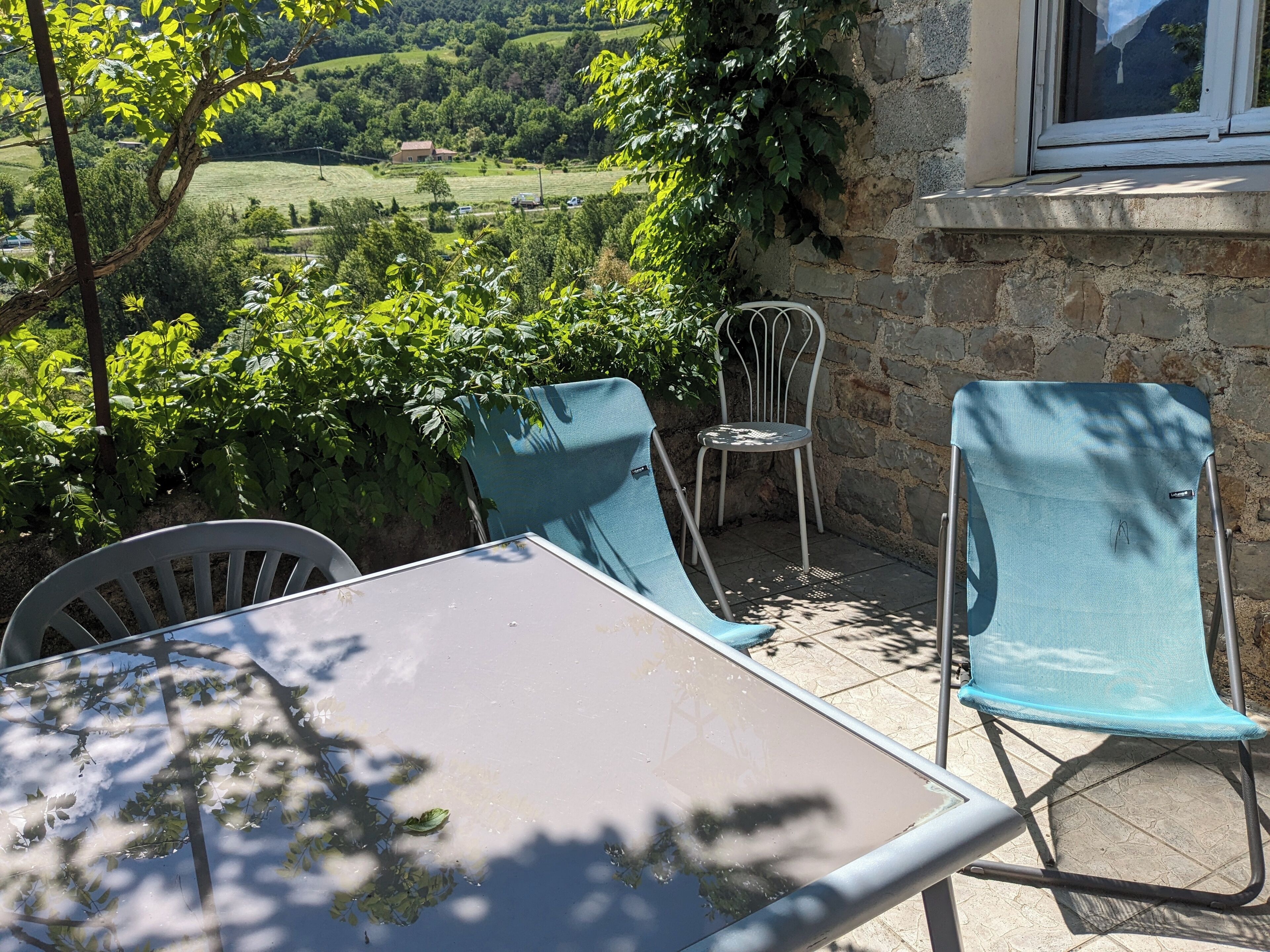 An outdoor patio with a table and two chairs, overlooking a scenic landscape with hills and trees.
