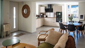 Una cocina moderna con armarios blancos, un comedor con una mesa redonda y sillas, y una sala de estar con un sofá y sillones.