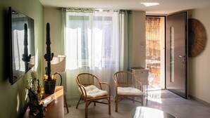 Una habitación con dos sillas de mimbre, una mesita, un espejo y vistas a un balcón con una puerta.
