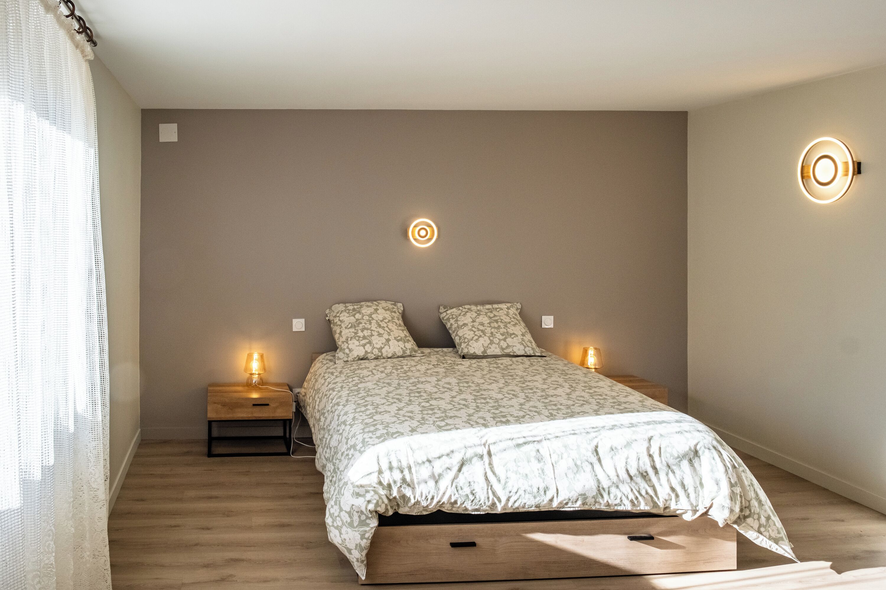 A bedroom with a bed, bedside tables, and wall-mounted lights.