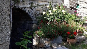 Edificio de piedra con un pequeño arco, rodeado de abundante vegetación y plantas en flor.