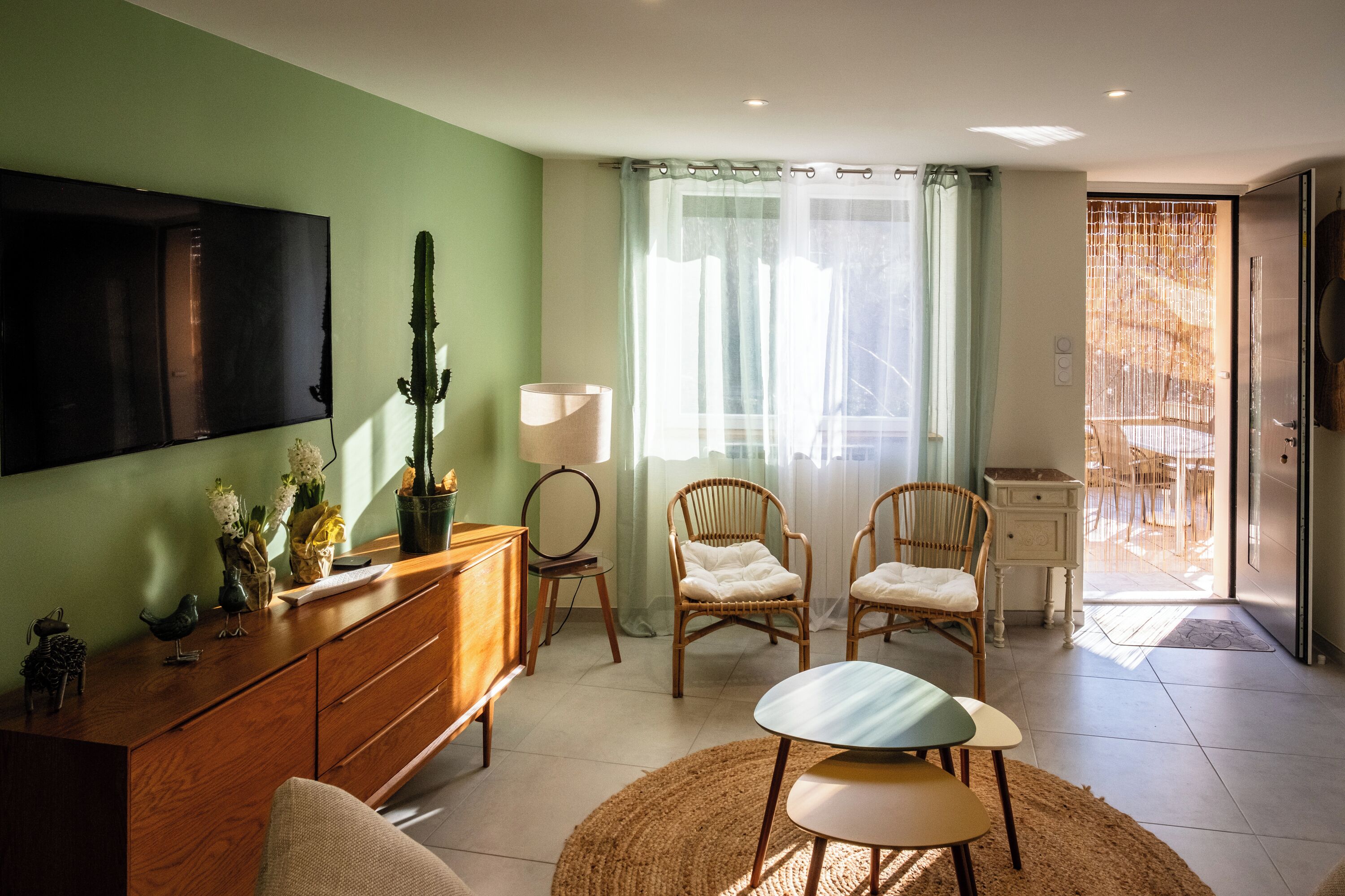 Ein Wohnzimmer mit Fernseher, Korbsesseln, einem Couchtisch und einem Essbereich, der durch eine Glastür sichtbar ist.