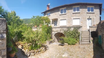 Una casa de piedra con una escalera de piedra que conduce a una puerta, rodeada de follaje y un cielo despejado.