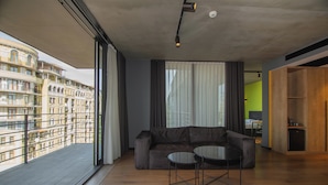 Un soggiorno moderno con un divano e un tavolino, ampie finestre con tende e un balcone con vista su un edificio.