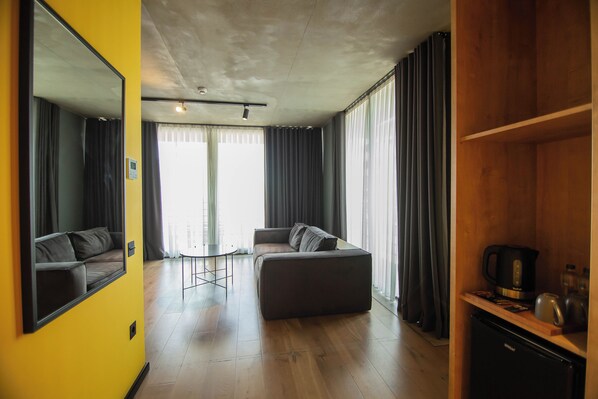 A modern living room with a sofa, a coffee table, and a kitchen area with a kettle and a microwave.