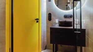 Un bagno con una porta gialla, uno specchio rotondo e un lavandino nero.
