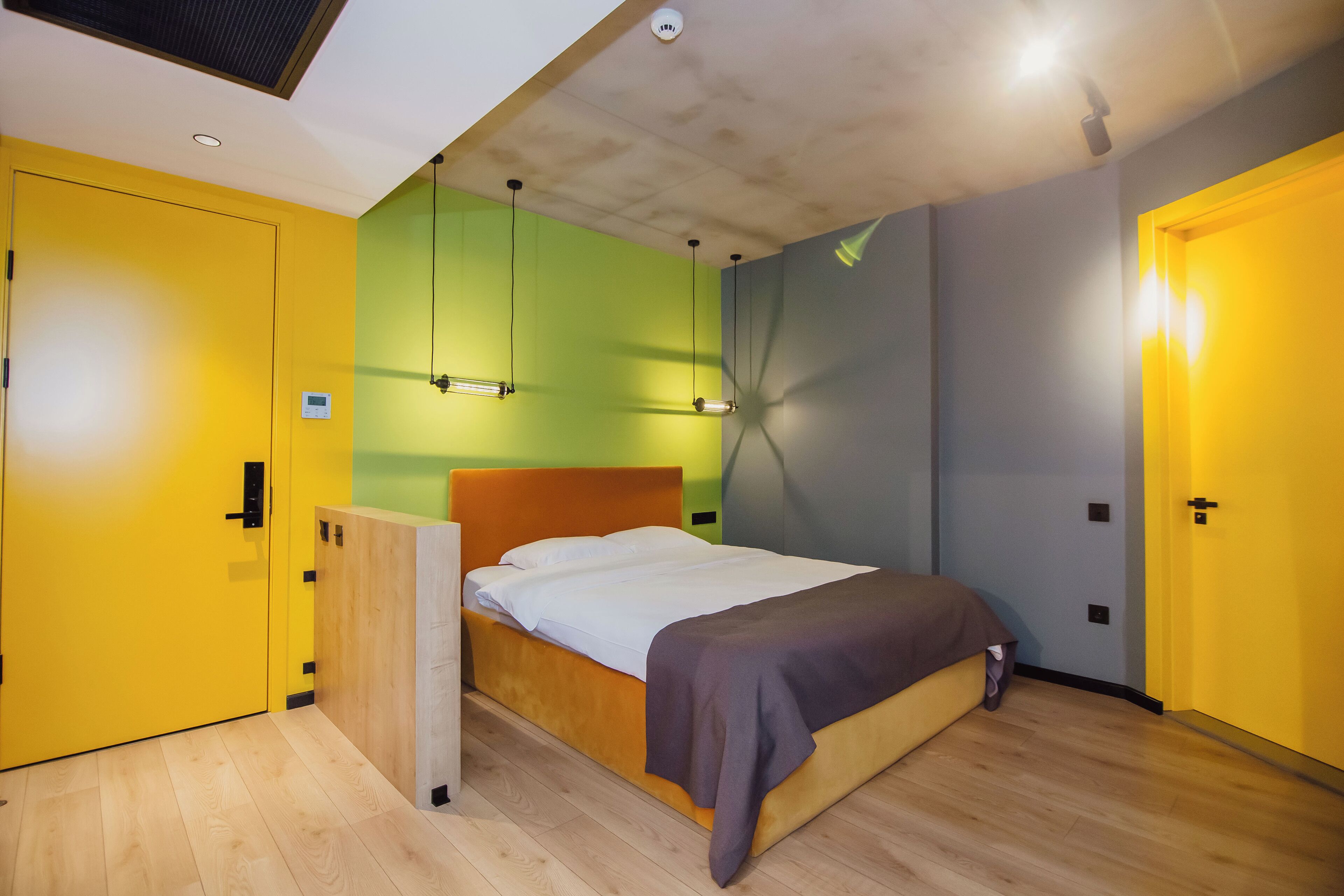 Un dormitorio moderno con suelo de madera, cama con cabecera marrón y paredes pintadas de amarillo y verde.