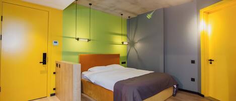 Un dormitorio moderno con suelo de madera, cama con cabecera marrón y paredes pintadas de amarillo y verde.