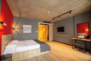 Ett modernt hotellrum med en säng, ett skrivbord, en stol och en tv.