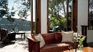 Un salon moderne avec un canapé en cuir, une table basse en bois et une vue sur un lac et des arbres.