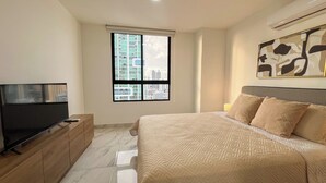 Un dormitorio con cama, televisión, ventana y un cuadro en la pared.