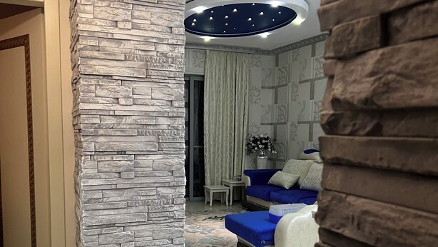 Un salon moderne avec un mur d’accent en pierre, un canapé bleu et un luminaire suspendu au plafond.